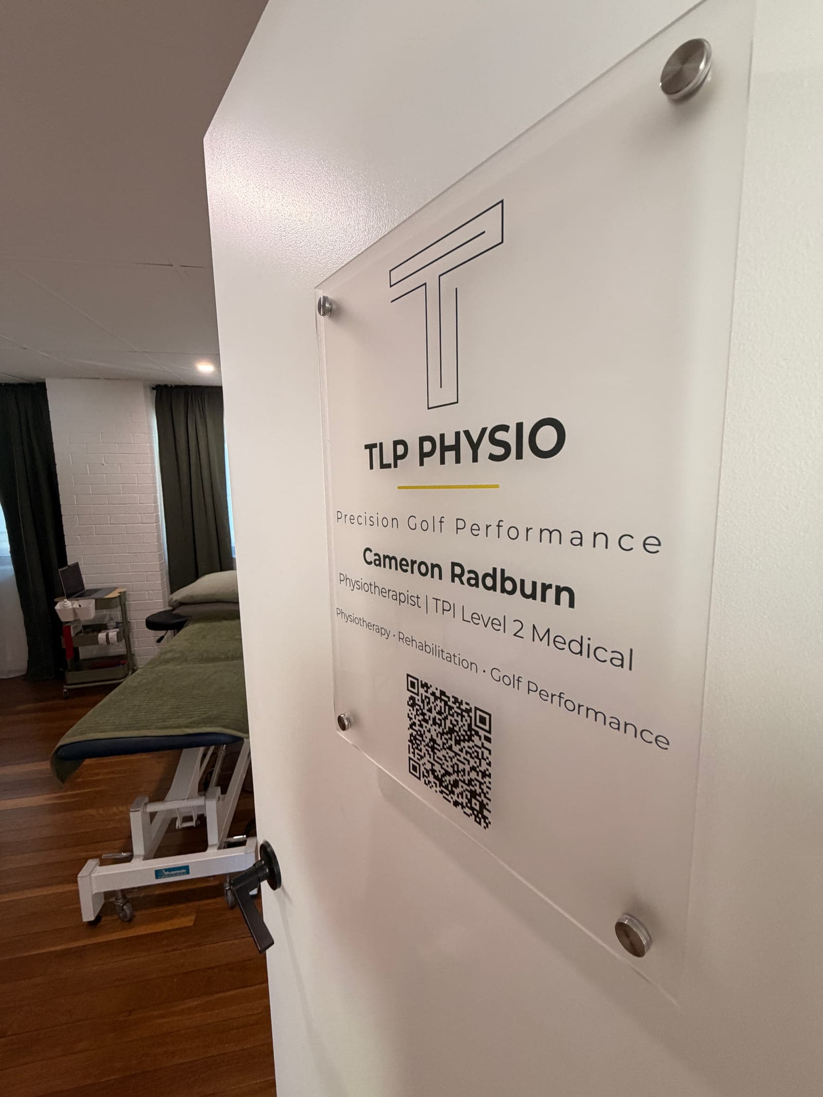 The TLP Physio sign on the treatment room door inside Never Quit South Brisbane, listing Cameron Radburn’s name and TPI Level 2 Medical certification — look for this door on arrival.